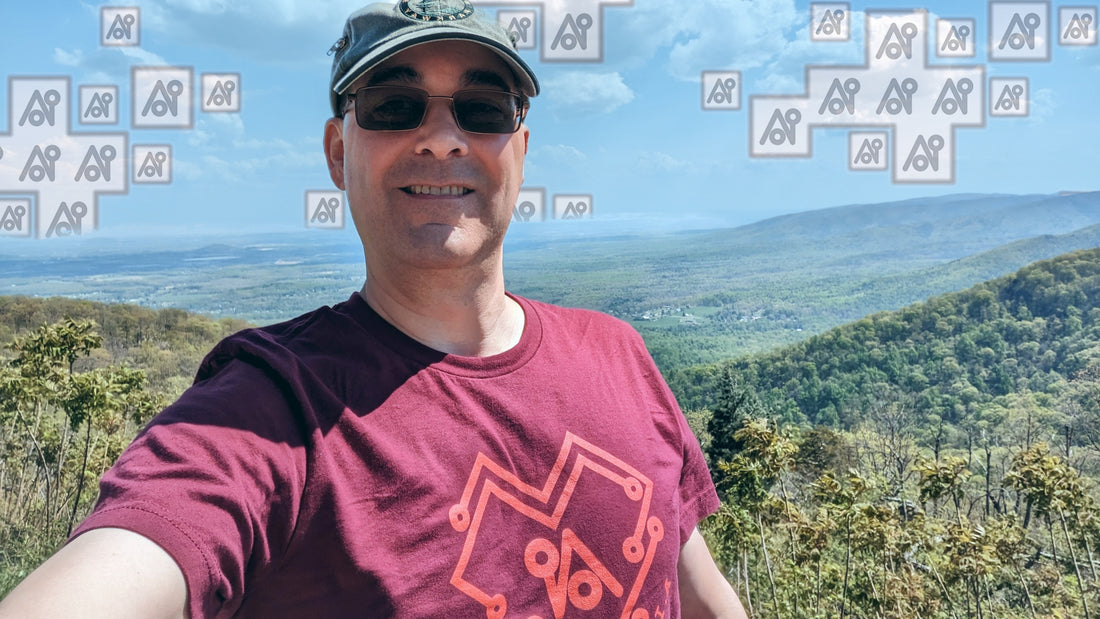 The author is wearing an AI symbol t-shirt and is taking a selfie with a mountaintop view of a valley where AI-symbol clouds are replacing clouds.